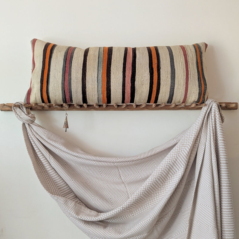 Decorative pillow with striped pattern on a wooden rack against a white wall.