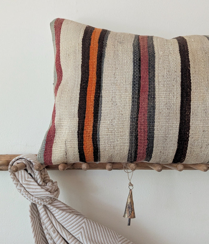 Decorative pillow with striped pattern on a wooden rack against a white wall.