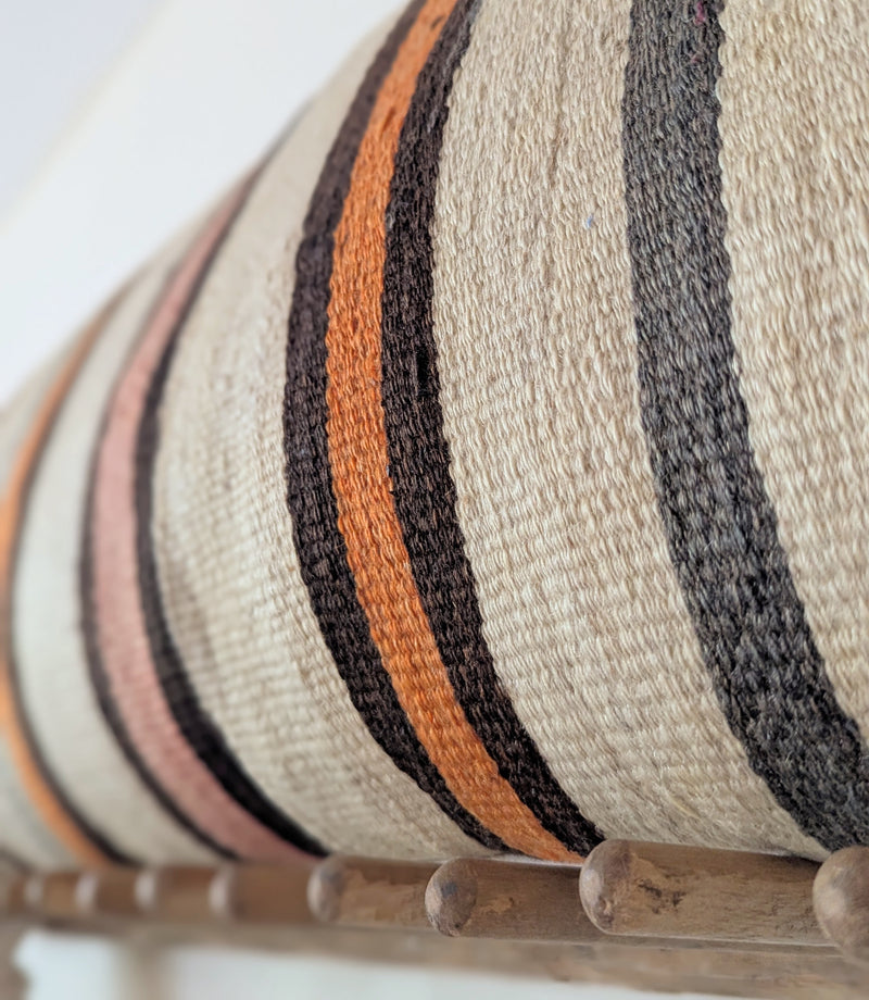 Close up of a decorative pillow with striped pattern on a wooden rack against a white wall.