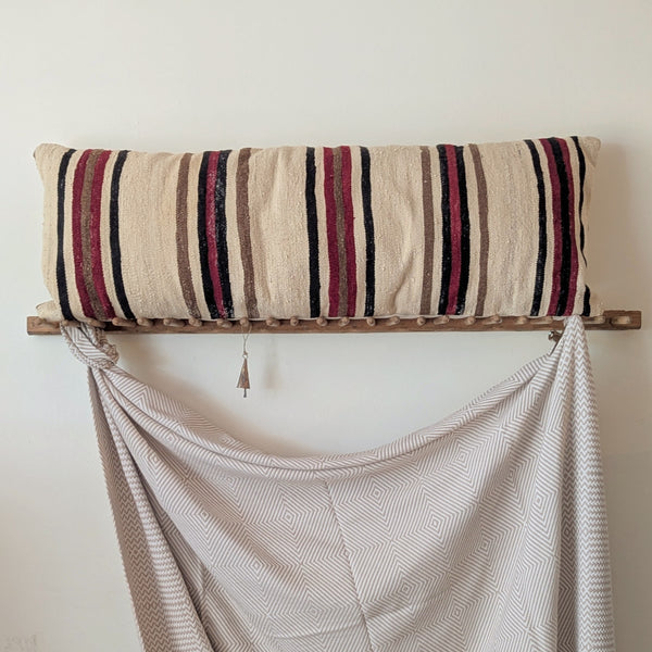 Striped pillow on a wooden shelf with a draped fabric against a white wall