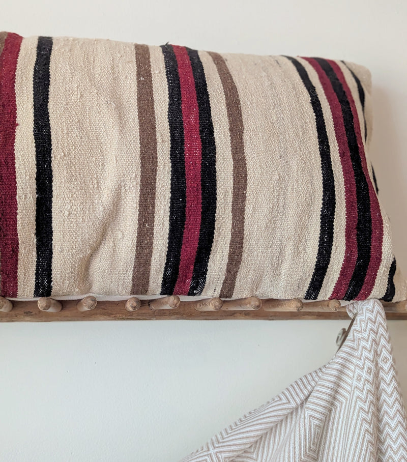 Striped pillow on a wooden shelf with a draped fabric against a white wall