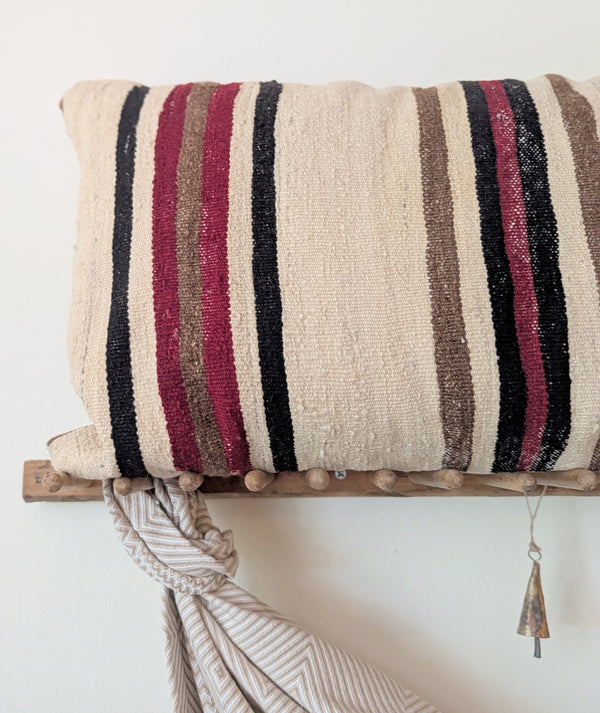 Striped pillow on a wooden shelf with a draped fabric against a white wall