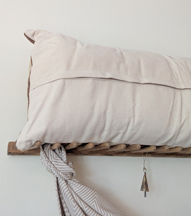 Beige pillow on a wooden shelf against a white wall