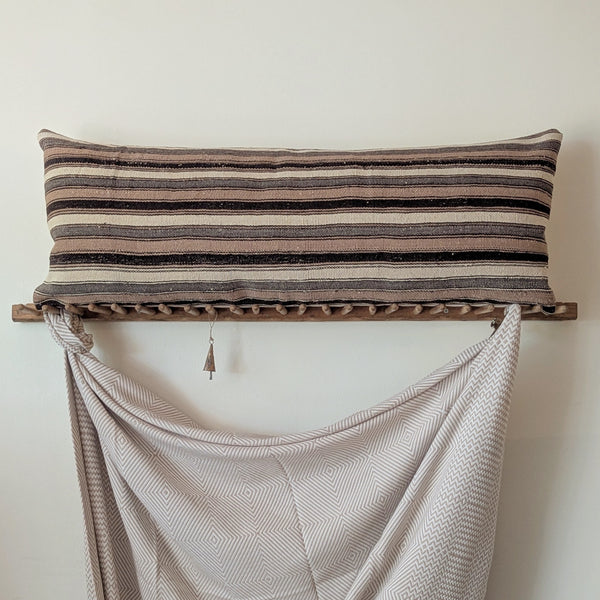 Striped pillow on a wooden rack with a draped blanket against a plain wall