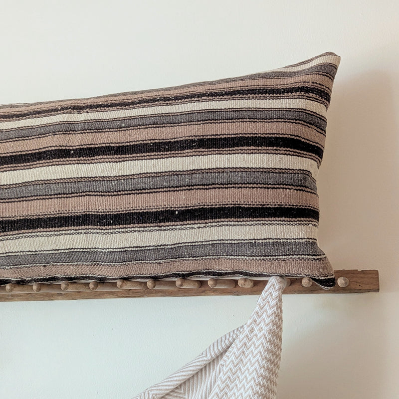 Striped pillow on a wooden rack with a draped blanket against a plain wall