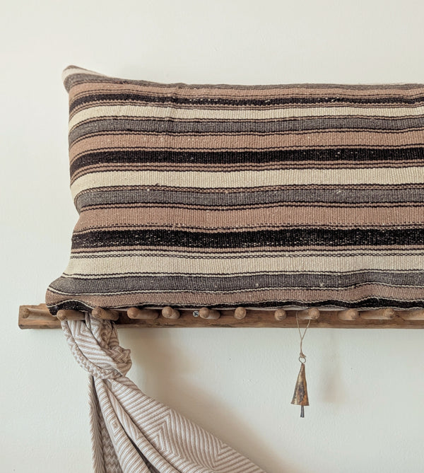 Striped pillow on a wooden rack with a draped blanket against a plain wall