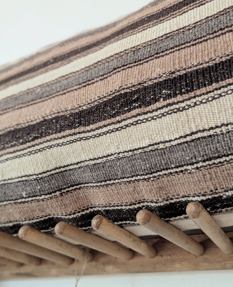 Striped pillow on a wooden rack with a draped blanket against a plain wall