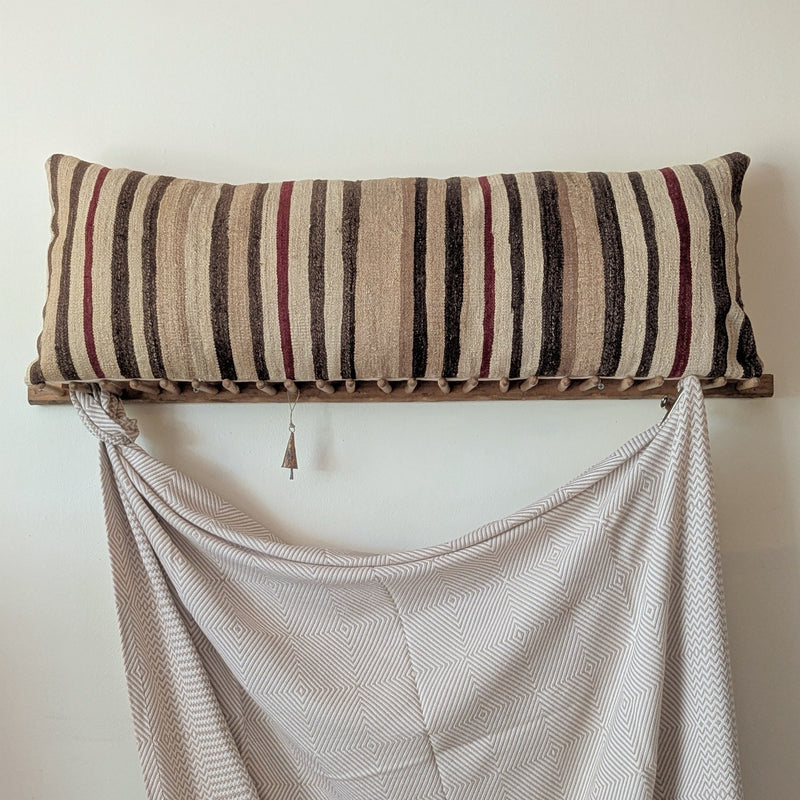 Striped pillow on a wooden stand with a draped fabric in the foreground against a plain wall.