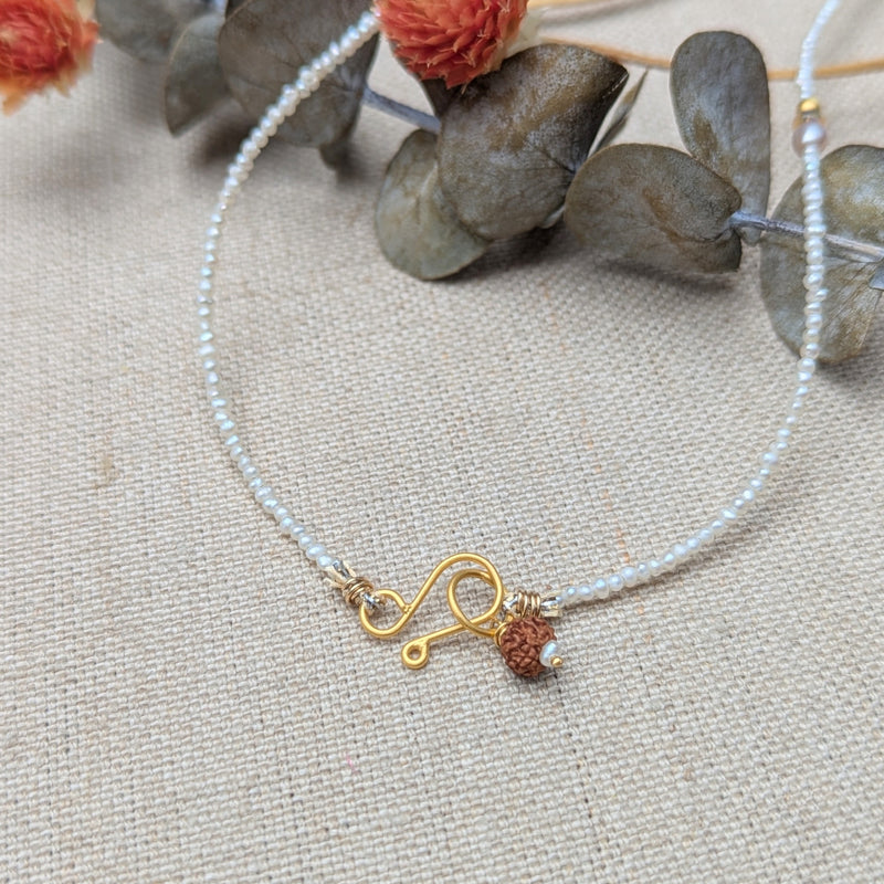 Delicate necklace with a gold clasp and brown seed bead on pearl beaded cord on a textured fabric background