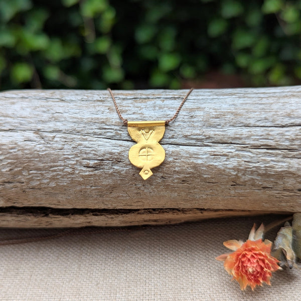 Gold necklace with a pendant and a brown cord on a wooden log with a blurred green background