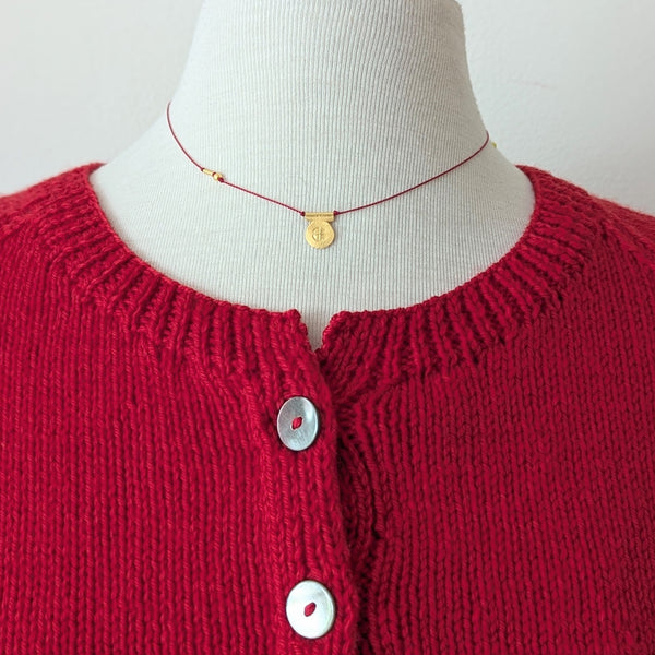 necklace with gold circular pendent with a textured design on a red cord on a mannequin with a Red knitted cardigan