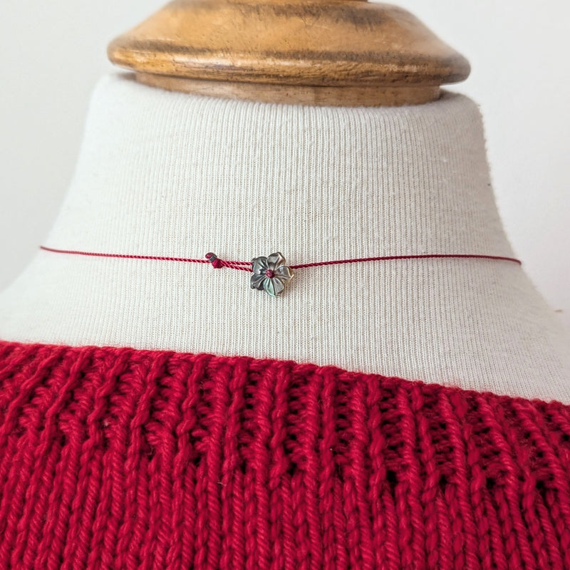 Necklace with a silver flower pendant clasp on a red cord on a mannequin wearing a red garment.