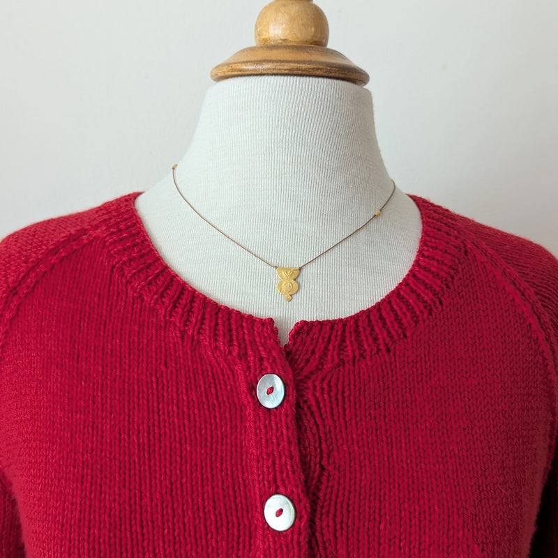 Gold pendent necklace with a textured design on a brown cord on a mannequin with a red knitted cardigan