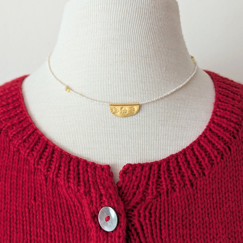 Necklace with a half oval gold pendant with a textured design on a pearl beaded cordon a mannequin 
