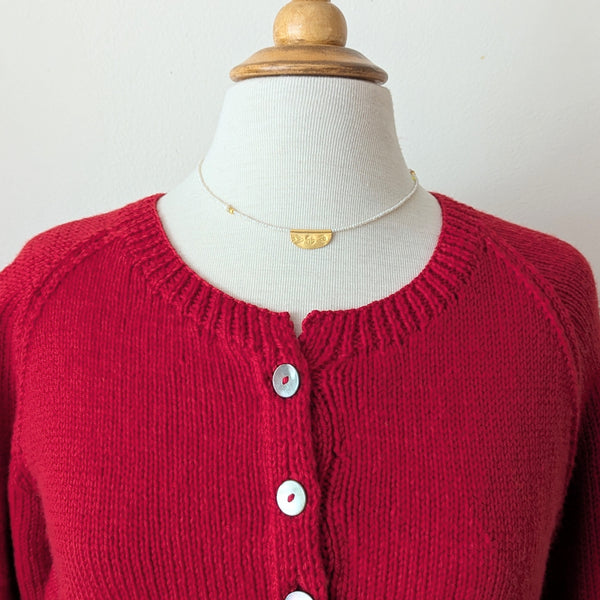 Necklace with a half oval gold pendant with a textured design on a pearl beaded cord on a mannequin with a plain background