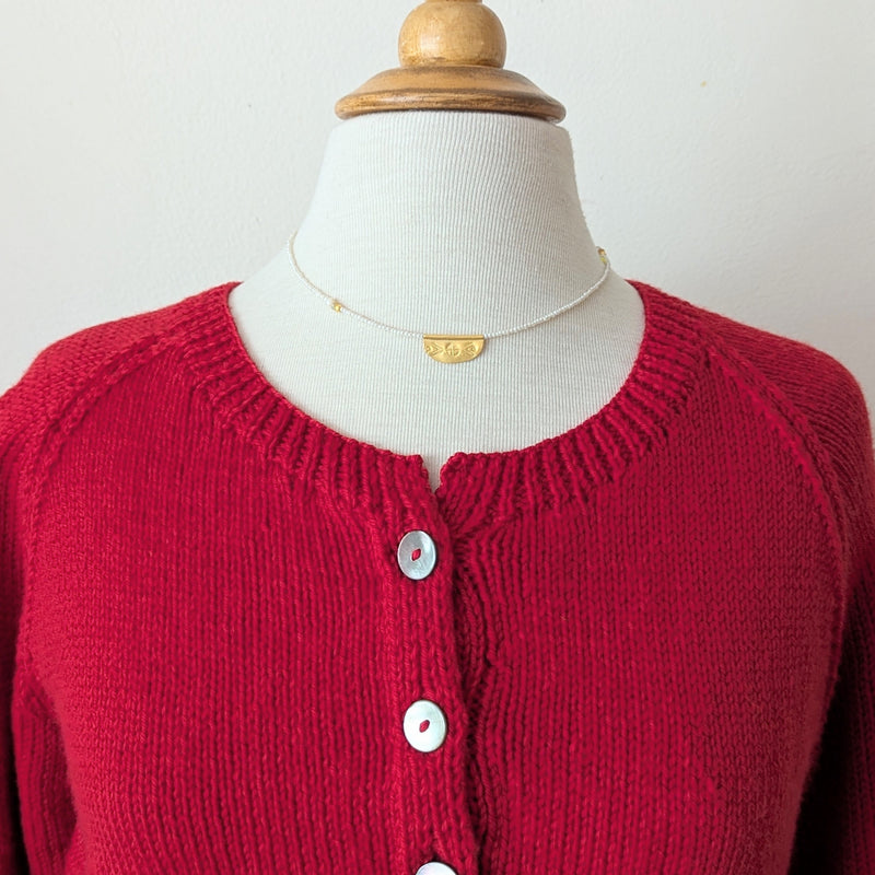 Necklace with a half oval gold pendant with a textured design on a pearl beaded cord on a mannequin with a plain background