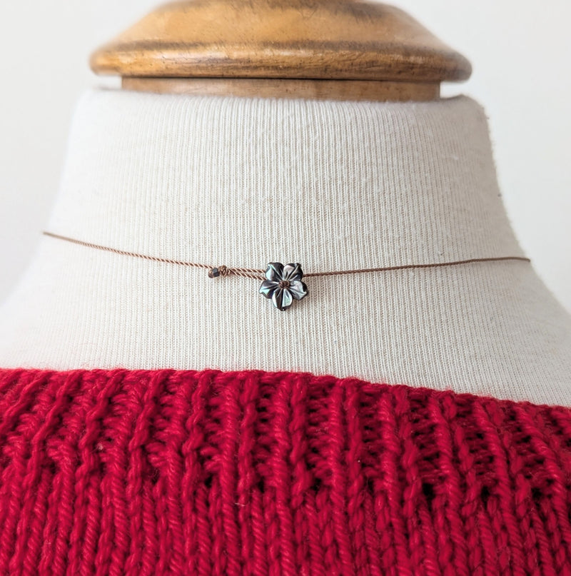 Necklace with a silver flower pendant clasp on a mannequin wearing a red sweater.