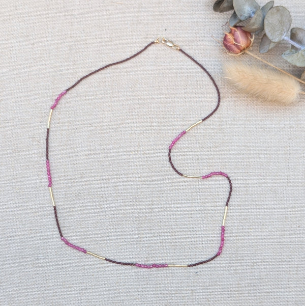 Ruby and gold beaded necklace on a light fabric background.