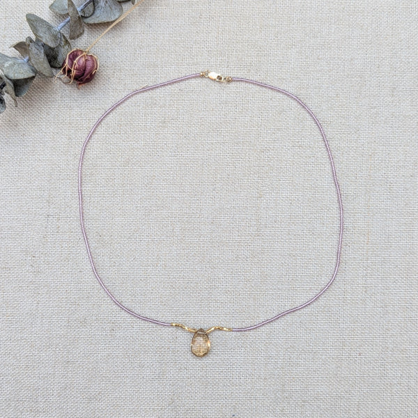 Lilac beaded necklace with a quartz pendant on a light gray background