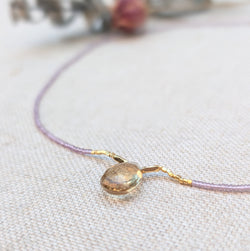 Liliac beaded necklace with a quartz pendant on a light fabric background