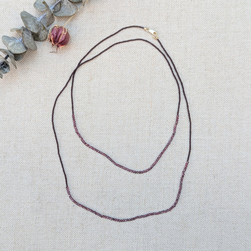Necklace with small ruby beads on a textured surface with decorative elements