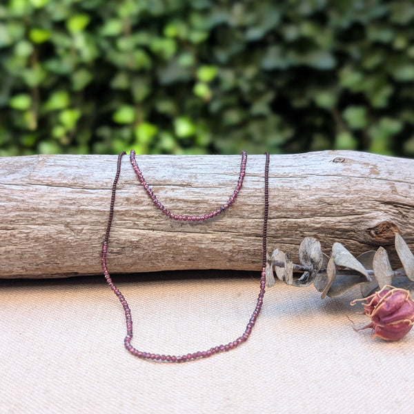 Necklace with small ruby beads on a piece of wood with a natural background