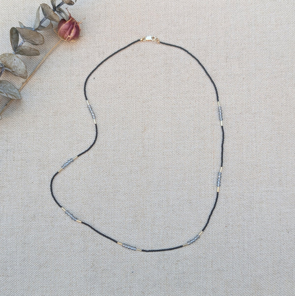 Necklace with black and grey beads and gold accents on a textured surface