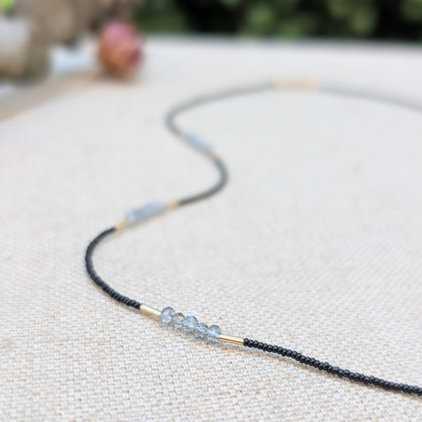 Necklace with black and grey beads and gold accents on a textured surface