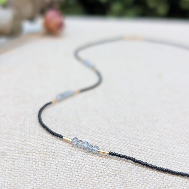 Necklace with black and grey beads and gold accents on a textured surface