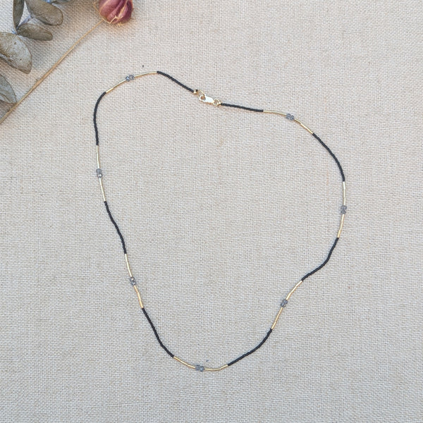 Necklace with black, grey, and gold beads on a textured surface