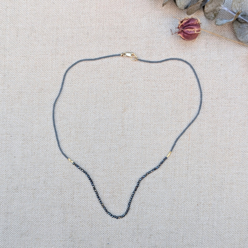 Necklace with small grey and black beads on a textured beige surface