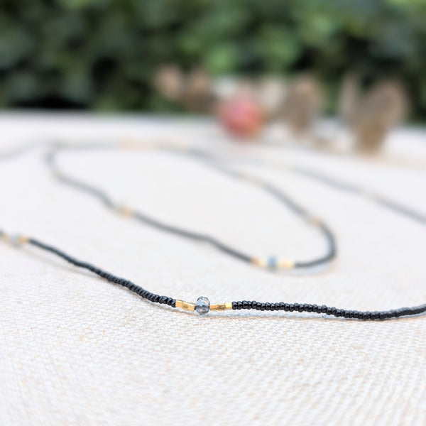 Black, grey, and gold beaded necklace on a textured surface with decorative elements