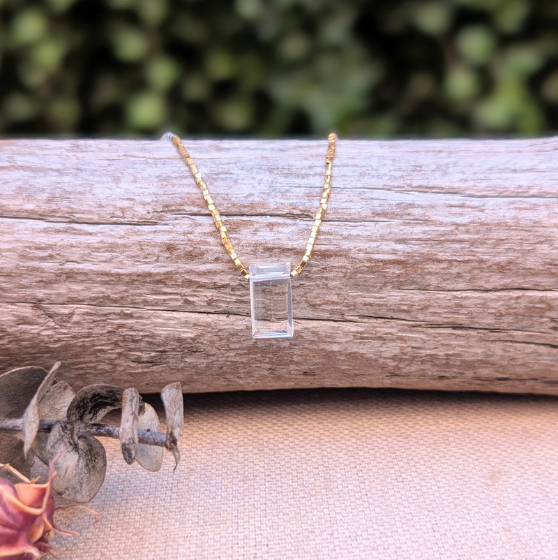 Gold necklace with a clear pendant on a wooden log with a blurred green background