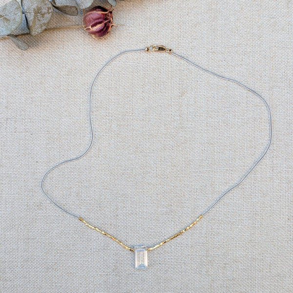 Clear and gold beaded necklace with a quartz pendant on a textured surface