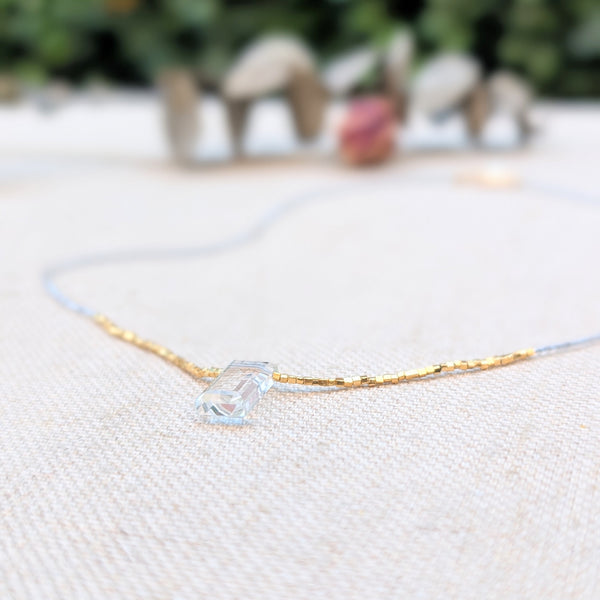 Clear and gold beaded necklace with a quartz pendant on a textured surface