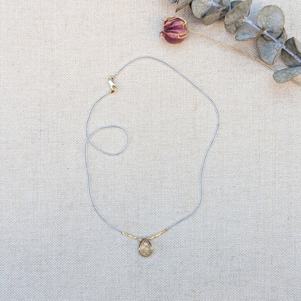 Clear and gold beaded necklace with a quartz pendant on a light fabric background.