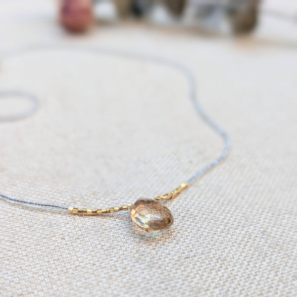 Clear and gold beaded necklace with a quartz pendant on a light fabric background.