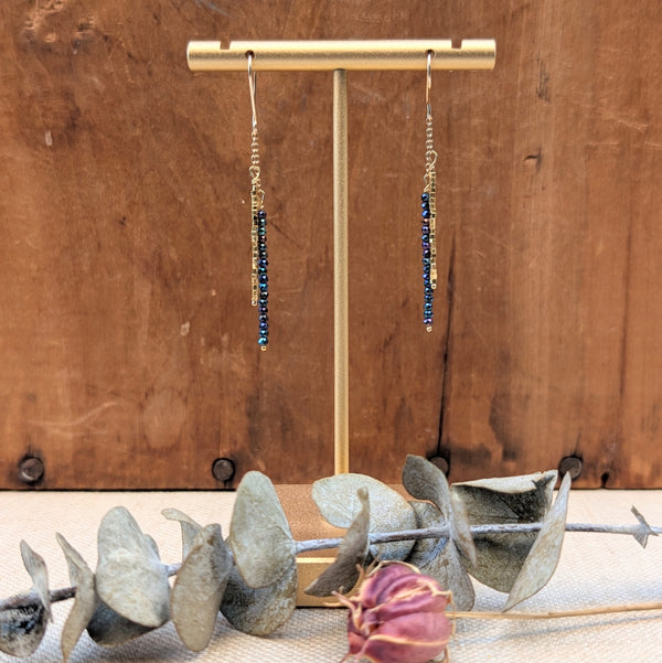 Gold earrings with blue/black stones on a gold stand against a wooden background