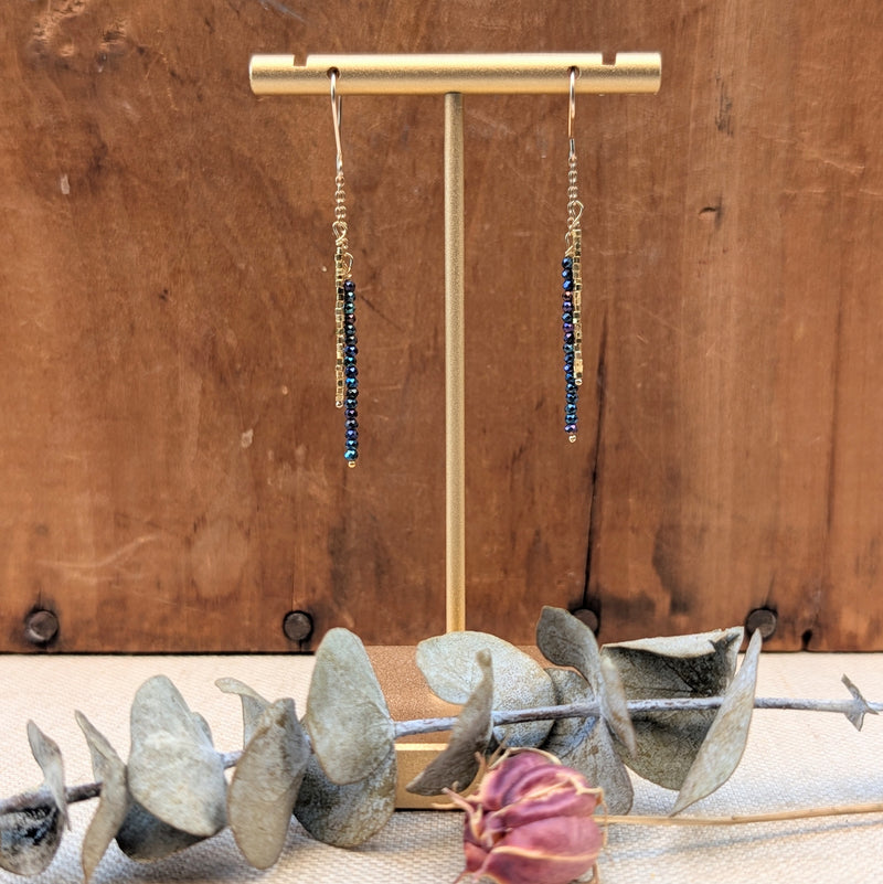 Gold earrings with blue/black stones on a gold stand against a wooden background