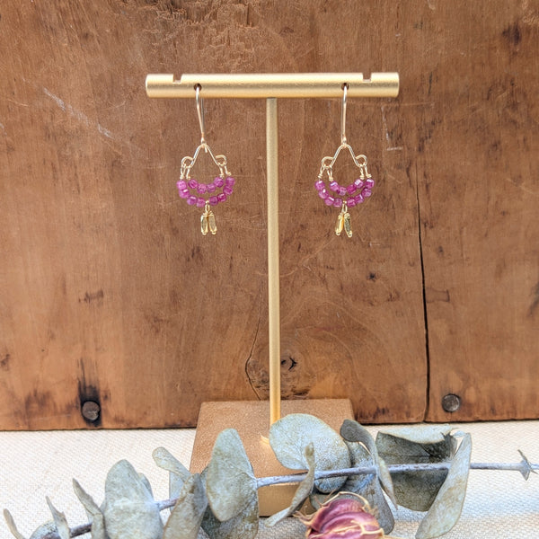 Pair of pink beaded earrings on a gold earring stand against a wooden background.