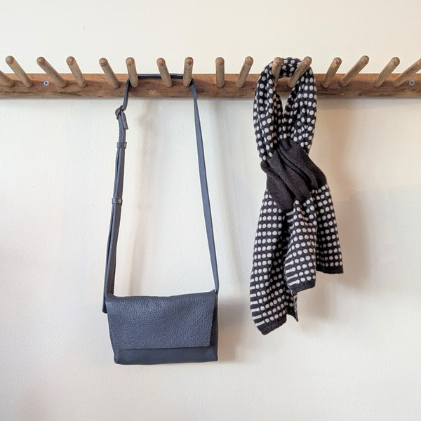 Blue Stitch and Tickle mini messenger crossbody bag and checkered scarf hanging on a wooden rack against a white wall.