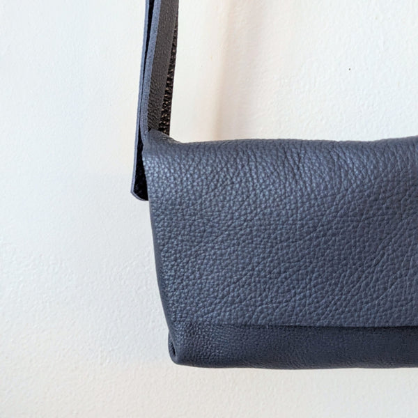 Blue Stitch and Tickle mini messenger crossbody bag hanging on a wooden rack against a white wall.