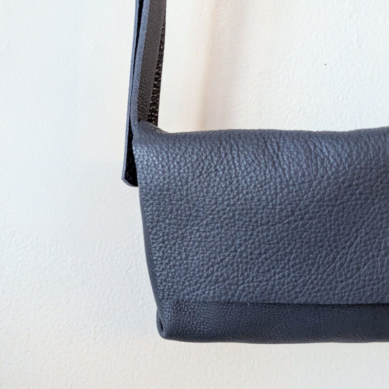 Blue Stitch and Tickle mini messenger crossbody bag hanging on a wooden rack against a white wall.