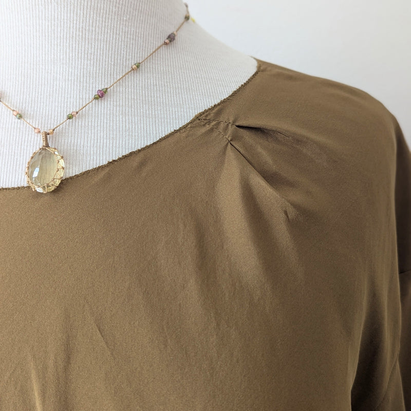 Tobacco brown draped silk blouse from Susanne Bommer on a mannequin with a necklace featuring a large gemstone pendant.