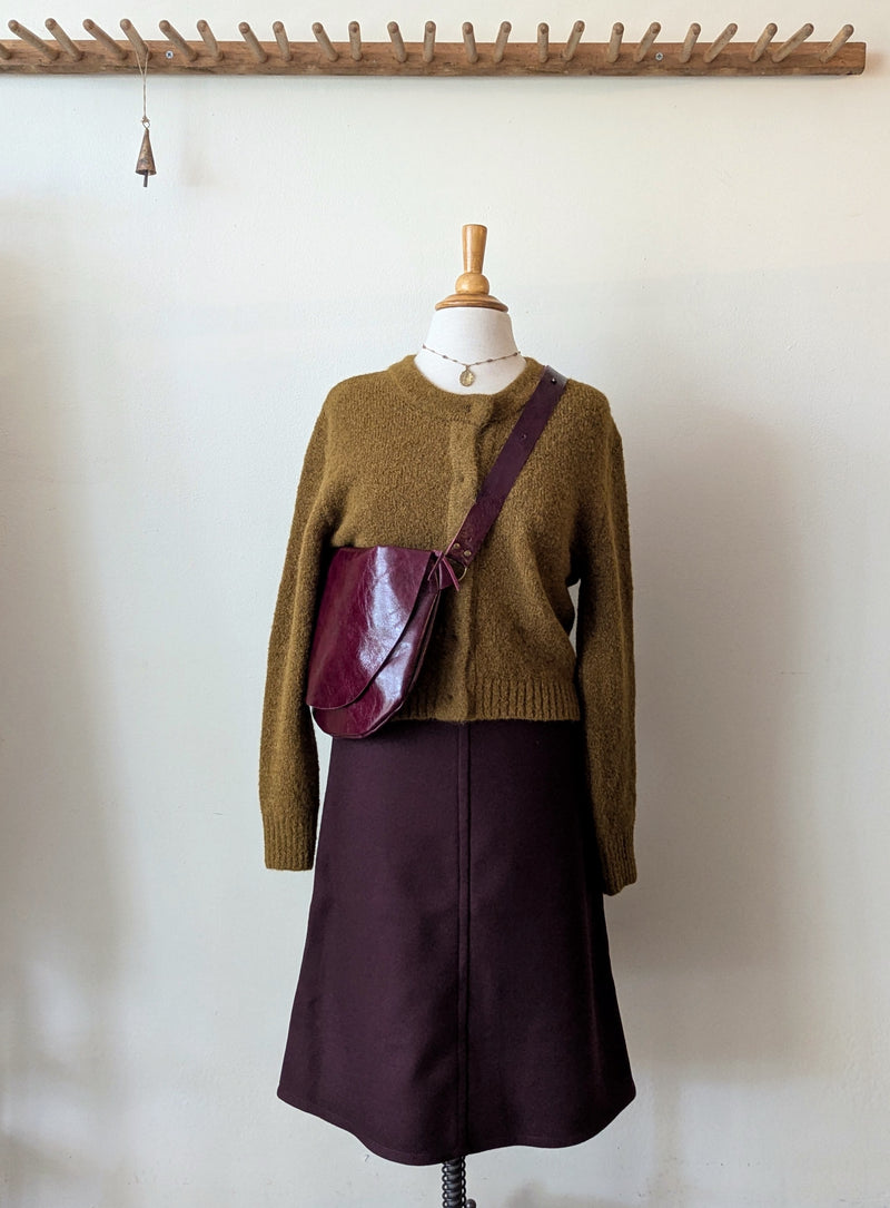 Mannequin wearing a brown long-sleeve cardigan and bordeaux skirt from Susanne bommer with a matching stitch & tickle bag against a plain background