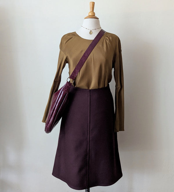 Mannequin wearing a brown long-sleeve top and bordeuc skirt from Susanne bommer with a matching stitch & tickle bag against a plain background
