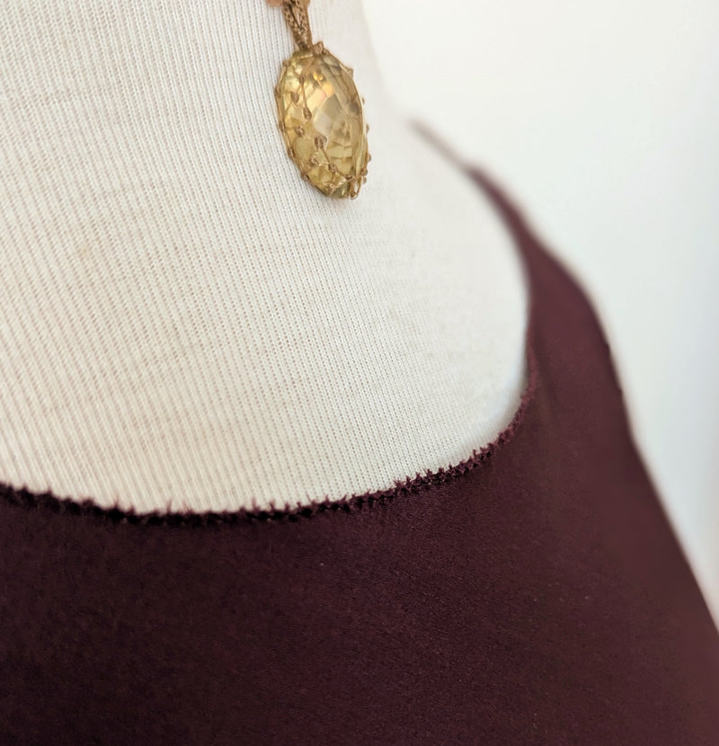 Close-up of a gold pendant on a mannequin with a white and purple garment.