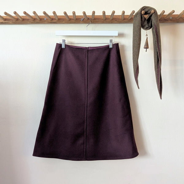 Bordeaux wool Susanne Bommer skirt hanging on a wooden rack against a white wall