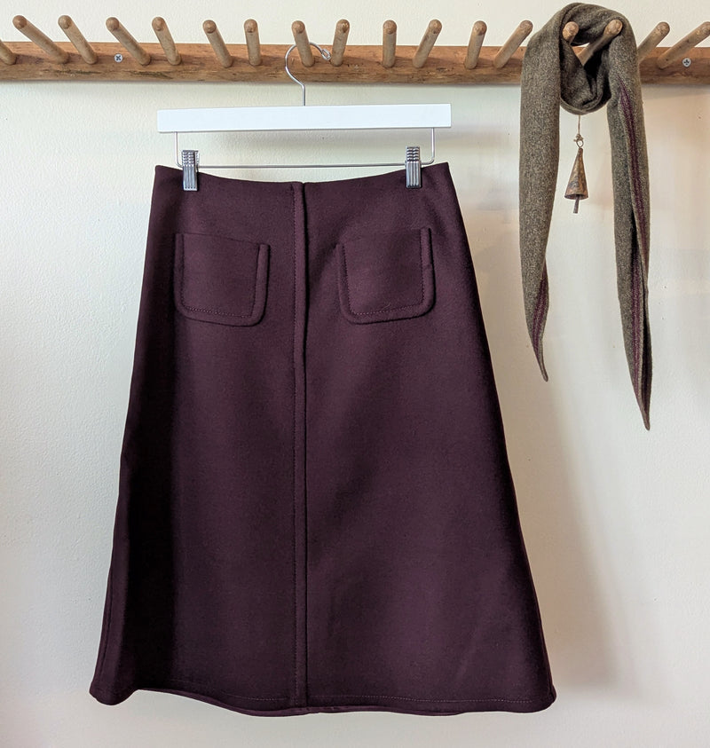 Back of the wool pocket Susanne bommer skirt with twot pockets hanging on a rack against a white wall.