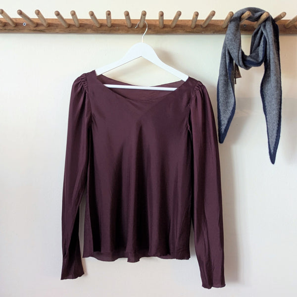 Susanne Bommer puff sleeve bordeaux long-sleeve top on a hanger with a gray scarf in the background.